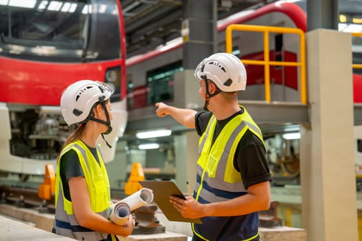 Professional engineer man point to electric train in the back and discuss with factory worker about check and maintenance the system in workplace area.