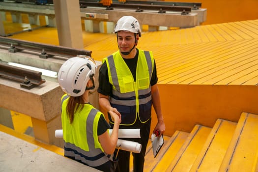 Two engineer or technician workers man and woman stand on step in area of factory workplace to discuss about their work.