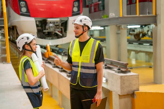 Professional technician worker man stand and talk about work to engineer or coworker woman in front of electric train in factory workplace or maintenance center.