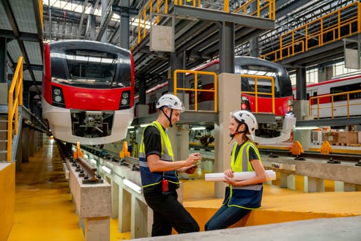 Technician or engineer workers man and woman stay in front of electric train and they look happy during work or relax in factory workplace.