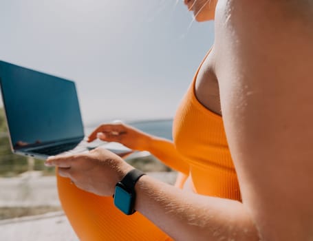 Digital nomad, Business woman working on laptop by the sea. Pretty lady typing on computer by the sea at sunset, makes a business transaction online from a distance. Freelance, remote work on vacation