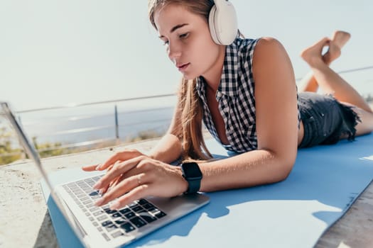 Digital nomad, Business woman working on laptop by the sea. Pretty lady typing on computer by the sea at sunset, makes a business transaction online from a distance. Freelance, remote work on vacation