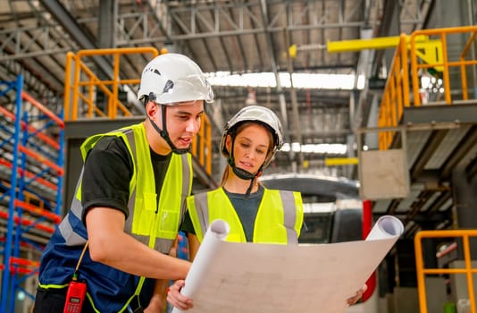 Close up professional engineer or technician workers man and woman concentrate to look the information in drawing paper and they stay in front of electric train in factory workplace.