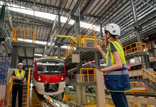 Back of technician or engineer work er woman point to the front of electric train and co-worker man stand beside of the train.