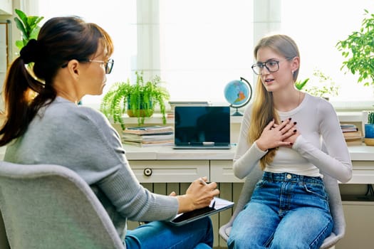 Young female teenager 16, 17 years old talking with counselor psychologist behavior social worker teacher, sitting in chair in office. Psychology psychotherapy therapy mental health adolescence youth