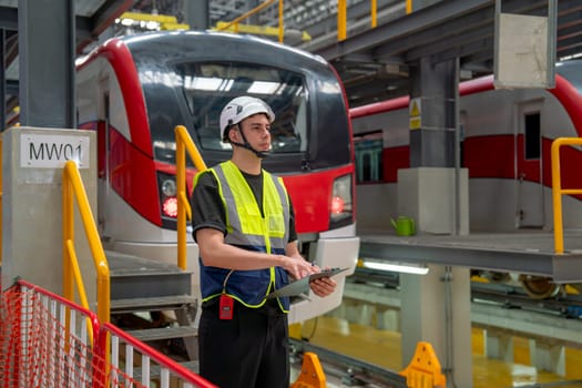 Professional engineer or technician worker man hold walkie talkie and archboard stand in front of electric train also look forward to right side in factory workplace or maintenance center.