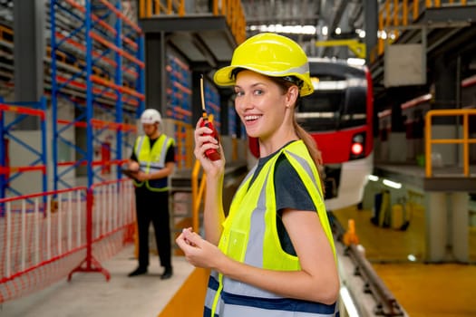 Professional engineer or technician worker woman hold walkie talkie and look at camera also stay in front of electric train in factory workplace or maintenance center.
