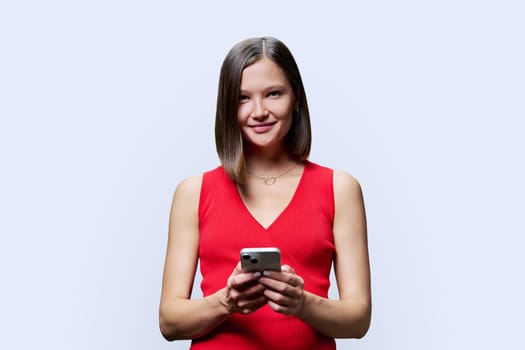 Young woman with smartphone in hands on white studio background. Smiling successful fashionable female looking at camera. Using mobile applications for work business shopping banking study leisure