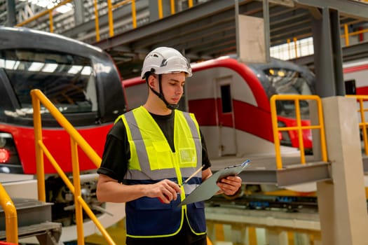 Professional engineer or technician worker man hold walkie talkie and archboard stand in front of electric train in factory workplace or maintenance center.