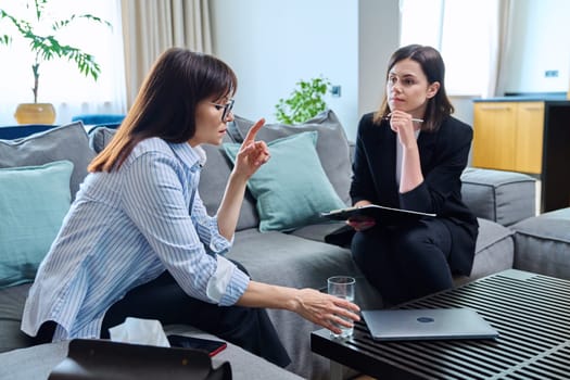 Female psychologist is having therapy session with middle-aged woman patient sitting on sofa in office. Psychology, psychotherapy, therapy, counseling, treatment, mental health concept