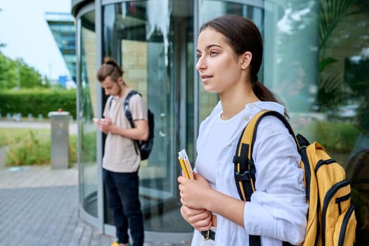 Portrait of high school student, smiling girl with backpack textbooks outdoor, educational building background. Adolescence, 15, 16, 17 years old, lifestyle, education concept