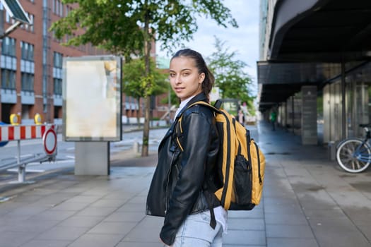 Portrait of teenage high school student, smiling confident girl 16, 17 years old with backpack looking at camera outdoor, on street of modern city. Urban life, adolescence, education, youth concept