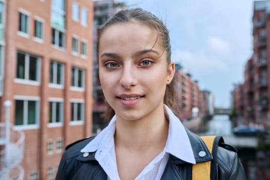 Portrait of teenage high school student, smiling confident girl 16, 17 years old with backpack looking at camera outdoor, on street of modern city. Urban life, adolescence, education, youth concept