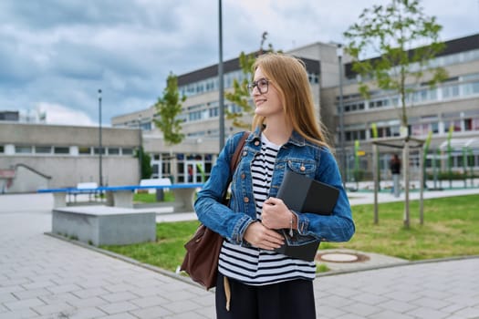 Girl student teenager outdoor near school building. Smiling teenage female with backpack digital tablet looking to the side, copy space. Adolescence, education, learning concept