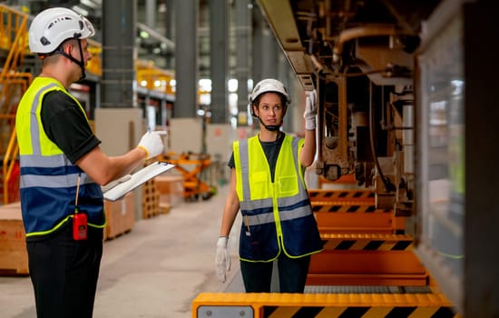 Professional engineer or technician worker woman check and discuss the problem of parts under electric train with co-worker man in workplace area.