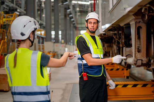 Technician or engineer worker point to the area of the problem to fix for electric train and discuss with co-worker or team staff woman also point to the same position.