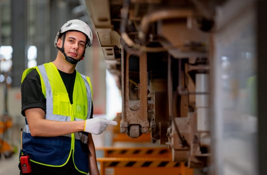 Portrait of engineer or technician worker point ot lower parts of electric train and also look at camera with confidence action in workplace area.