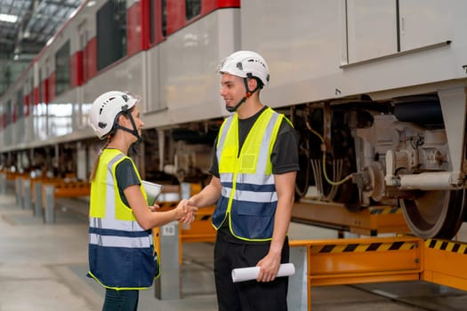 Professional engineer or factory technician worker man and woman shake hands for the success of joined project together in workplace near the electric train.