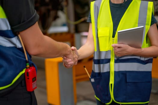 Close up engineer or factory technician worker man and woman shake hands in area of factory workplace.