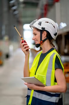 Vertical image of pretty factory worker woman use walkie talkie to contact with team or co-worker and also hold tablet also stay near the train with happiness for work.