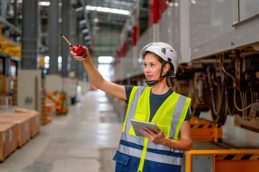 Professional technician or engineer worker woman hold tablet and use walkie talkie to point to left side and stay in factory industry workplace area.