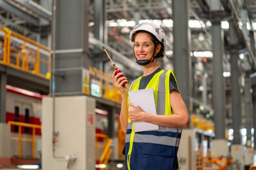 Portrait of professional engineer or technician worker woman hold tablet and walkie talkie also look at camera with smiling and stay in factory industry workplace area.