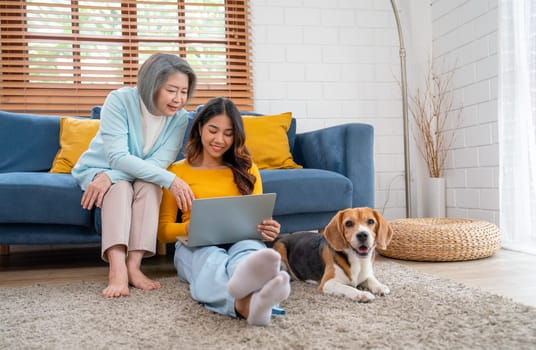 Asian senior and young woman enjoy with using laptop in living room and beagle dog also stay near and beside of them in the house with day light