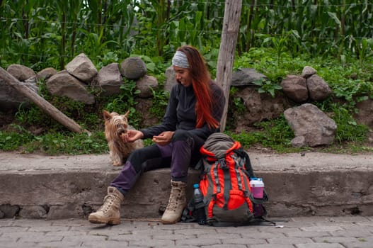 woman backpacker sitting on the sidewalk feeding her little dog some cookies and an orange backpack. High quality photo
