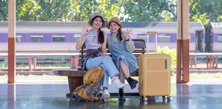 Two Asian female tourist friends are at the train station. Waiting for the train to travel to the provinces together on the weekend..