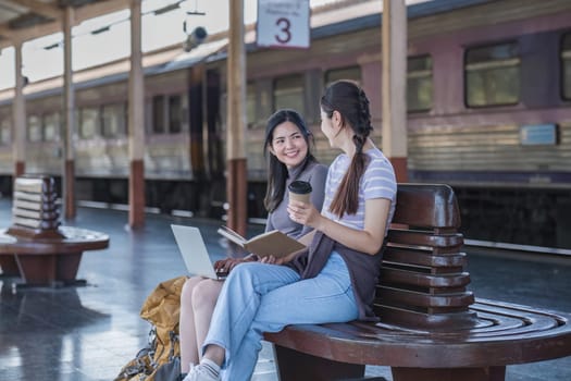 Two Asian female tourist friends are at the train station. Waiting for the train to travel to the provinces together on the weekend..