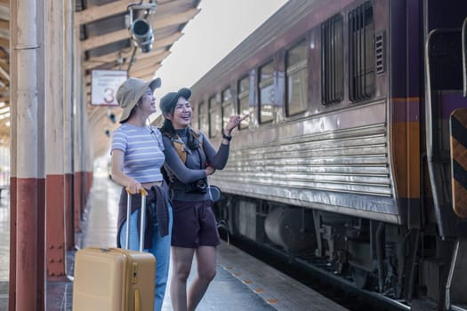 Two Asian female tourist friends are at the train station. Waiting for the train to travel to the provinces together on the weekend..