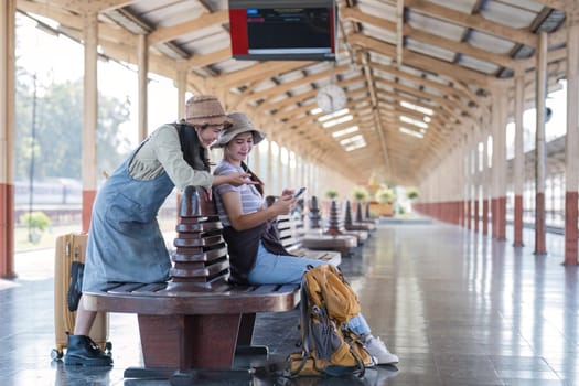 Two Asian female tourist friends are at the train station. Waiting for the train to travel to the provinces together on the weekend..