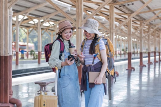 Two Asian female tourist friends are at the train station. Waiting for the train to travel to the provinces together on the weekend..