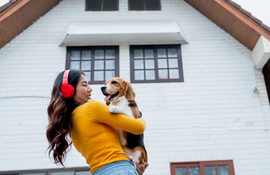 Young Asian girl with red earphone hold and hug beagle dog and stand in front of her house and she look happy with her pet.