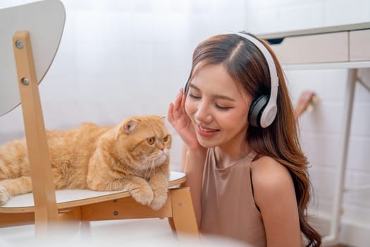 Pretty Asian woman with headphone sit on the floor near orange cat and she smile with happiness to stay and enjoy with her pet.