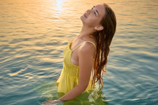 Close-up portrait of a young woman in a yellow dress at sunrise against the background of the sea. Woman walks on the seashore