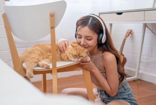 Pretty Asian woman with headphone sit on floor near bed and kiss to her cat with love and happiness.