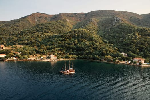 Sailboat sails across the bay against the backdrop of a resort town on the mountain coast. Drone. High quality photo