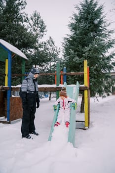 Mom looks at a little girl sliding down a snow-covered colorful slide. High quality photo