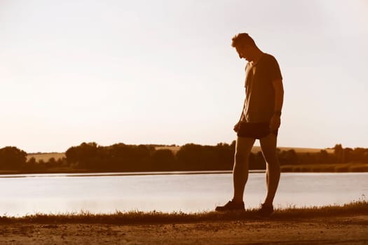 An athletic man jogging along the trails in a wheat field outside the city at sunset, a runner training in a picturesque outdoor area.