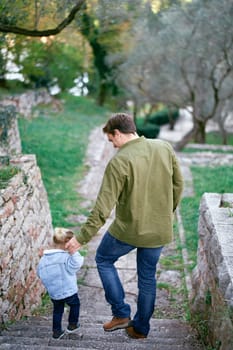 Dad and a little girl go down the stone steps, holding hands. Back view. High quality photo