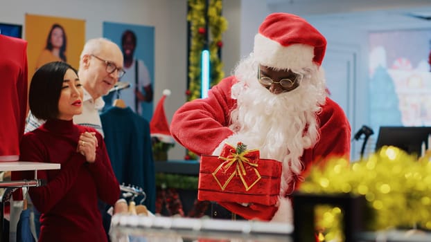 Worker wearing Santa Claus outfit in xmas ornate clothing store, inviting customers to participate in Christmas raffle competition in order to win promotional prize during festive holiday season