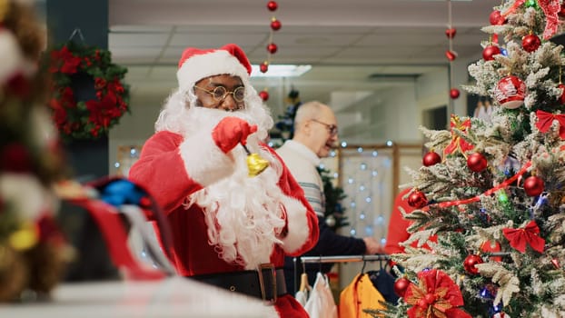 Employee acting as Santa Claus entertaining shoppers in Christmas decorated fashion store during winter holiday season. Worker instilling festive spirit in clients visiting clothing shop