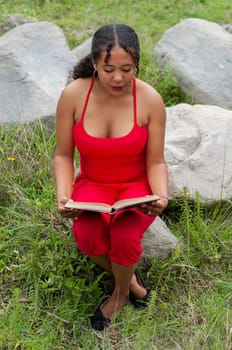 ecuadorian woman in a flashy dress quietly reading a book in nature next to some rocks. book day. High quality photo