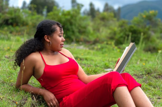 latina girl in red clothes lying on the lawn surrounded by nature with an open book in her hand. book day. High quality photo