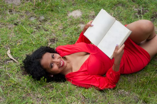 ecuadorian woman with black curly hair lying on the mountain in a red dress with an open book without text. book day. High quality photo