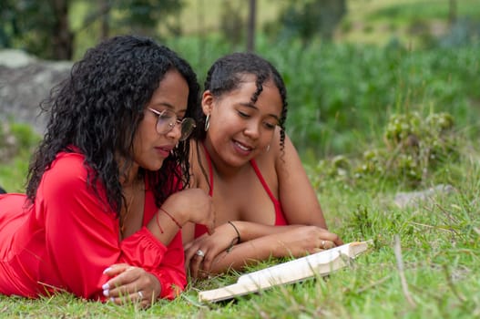 side copy space of two young Ecuadorian girls reading a book attentively on the grass surrounded by green nature. book day. High quality photo