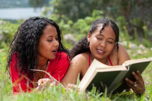 two young women from colombia with black curly hair reading a book lying on a mountain on a very sunny day. book day. High quality photo