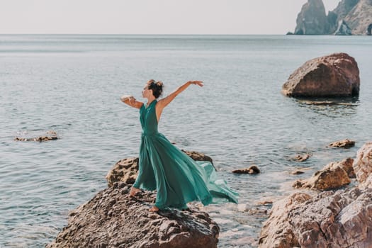 Woman green dress sea. Woman in a long mint dress posing on a beach with rocks on sunny day. Girl on the nature on blue sky background