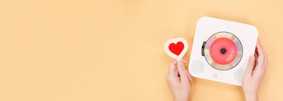 Hands holding white cd player with red disc and heart shape gift card on yellow background. Love music, Valentine day, Greeting, retro Love song, space for text